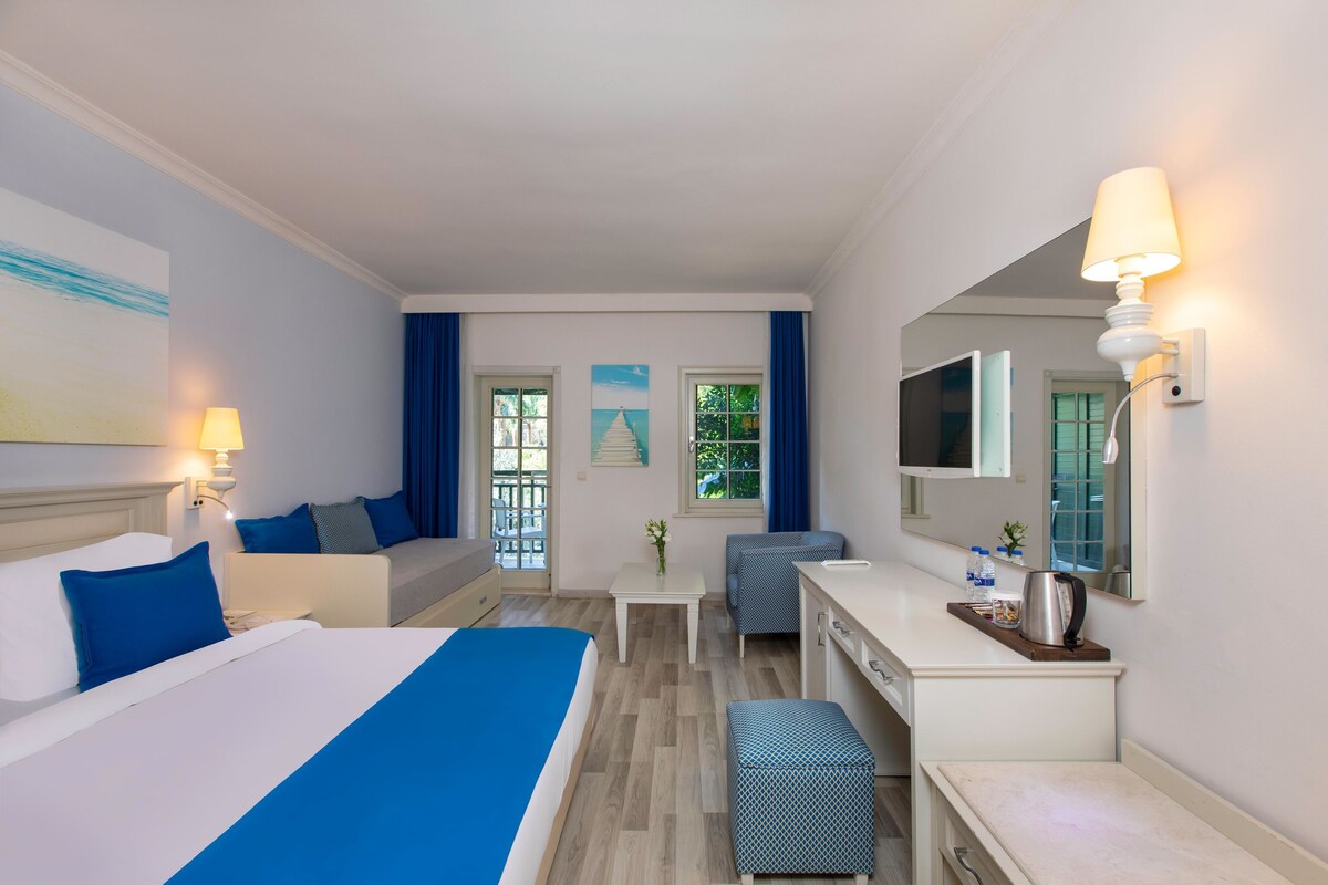 A hotel room with a bed, a desk, a chair, a small table, and a mirror.
