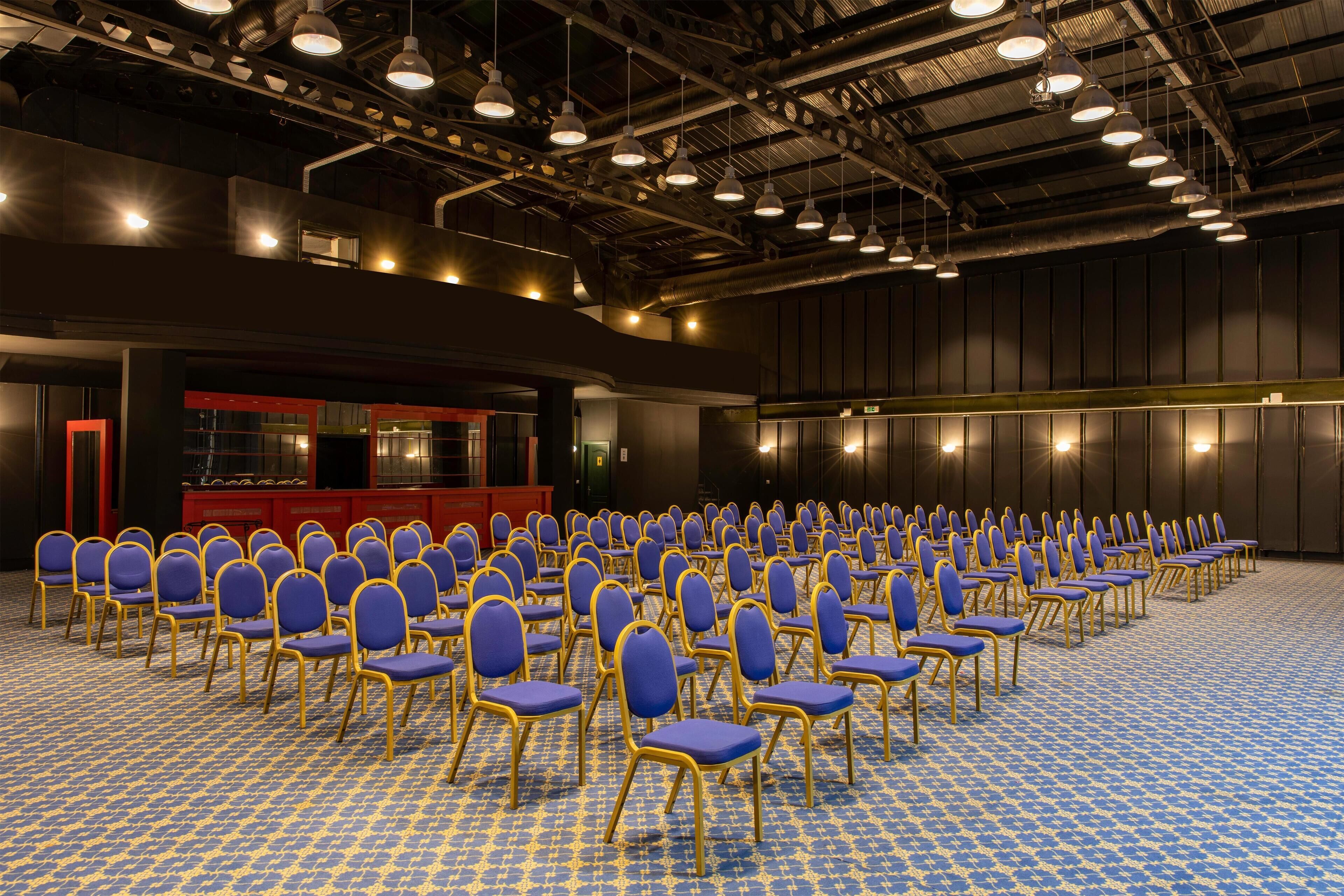 A conference room with rows of blue chairs and a red podium.
