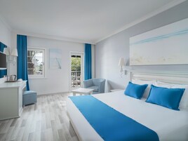 Habitación de hotel con una cama grande, un escritorio, una silla y un balcón con cortinas azules.