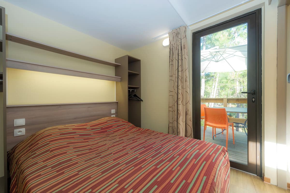 Habitación de hotel con cama, cabecera de madera, armario y balcón con mesa y sillas.