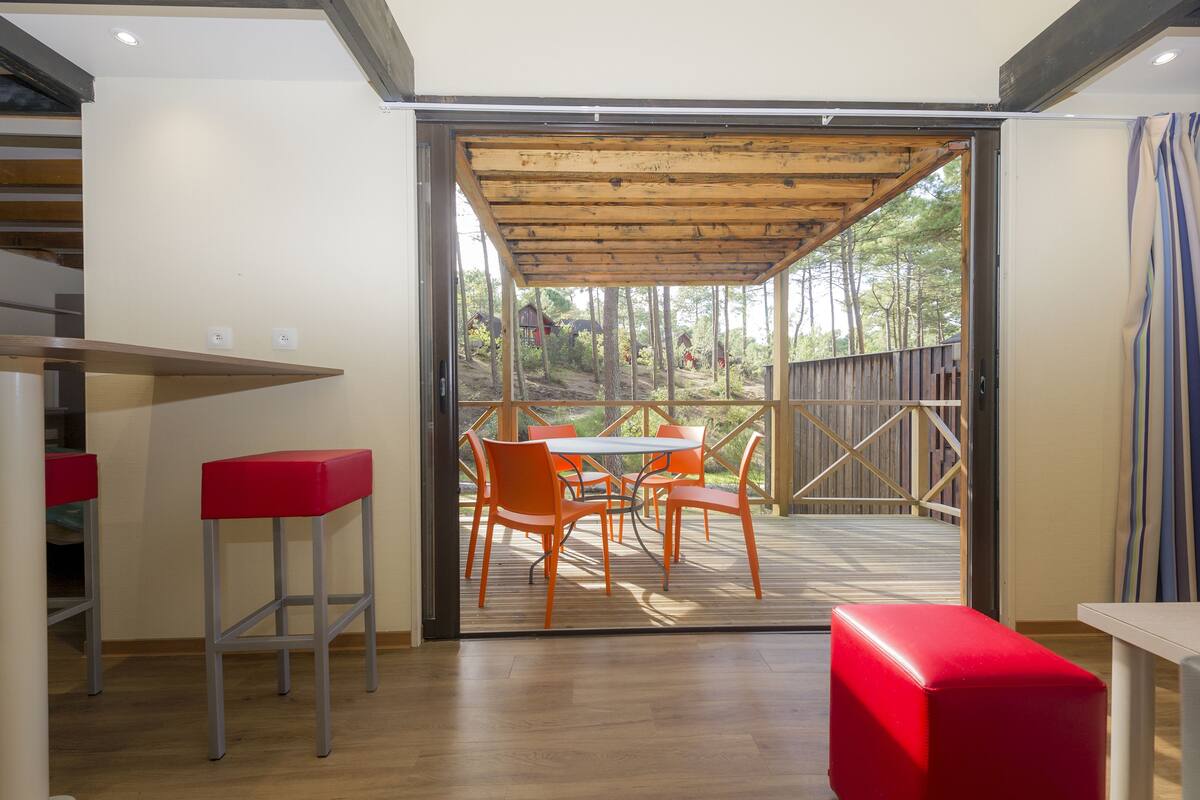 Un interior moderno con techo de madera, un comedor con sillas naranjas y una mesa, y un banco rojo.