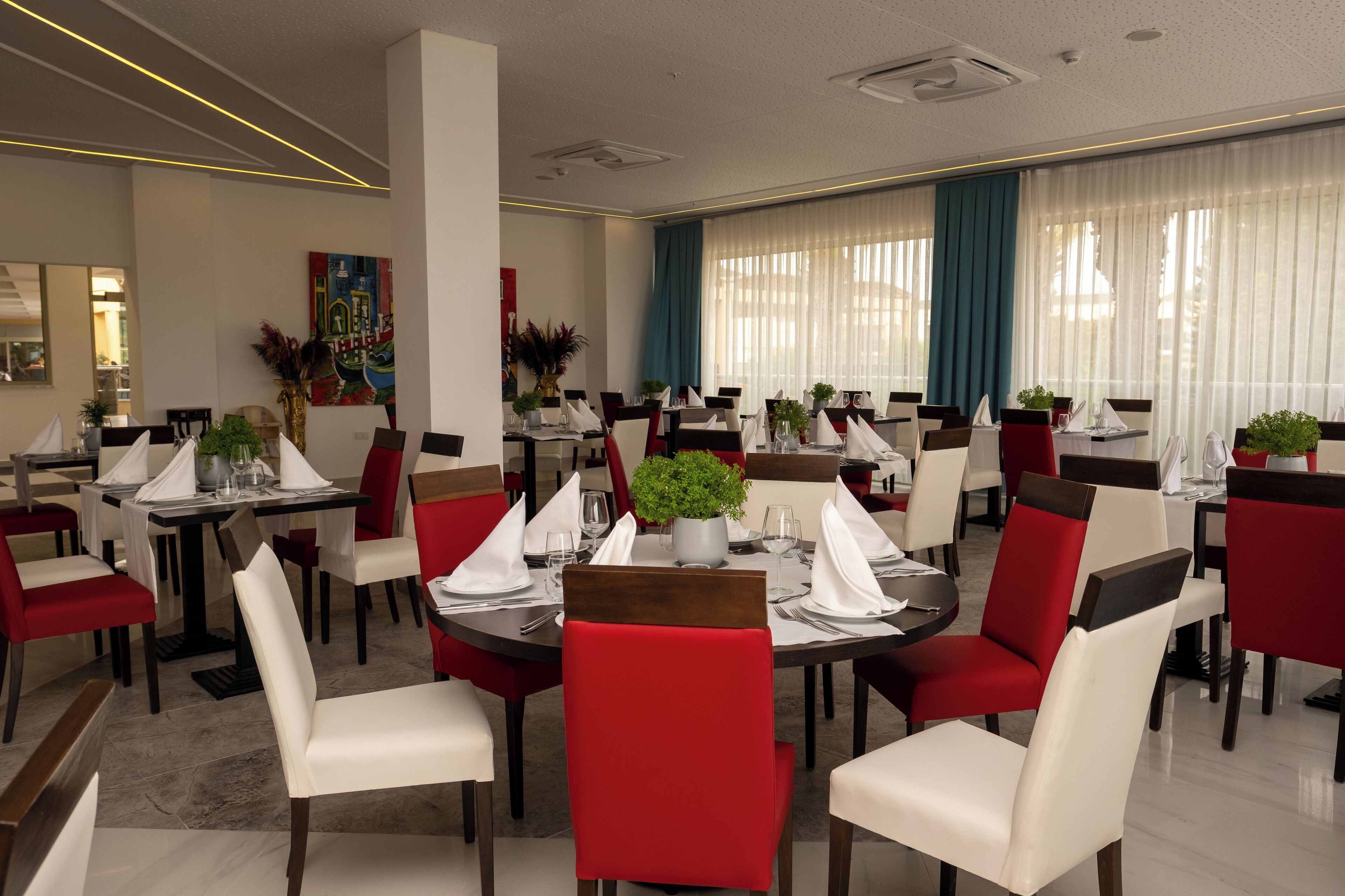 A modern dining area with round tables, red and white chairs, and potted plants.