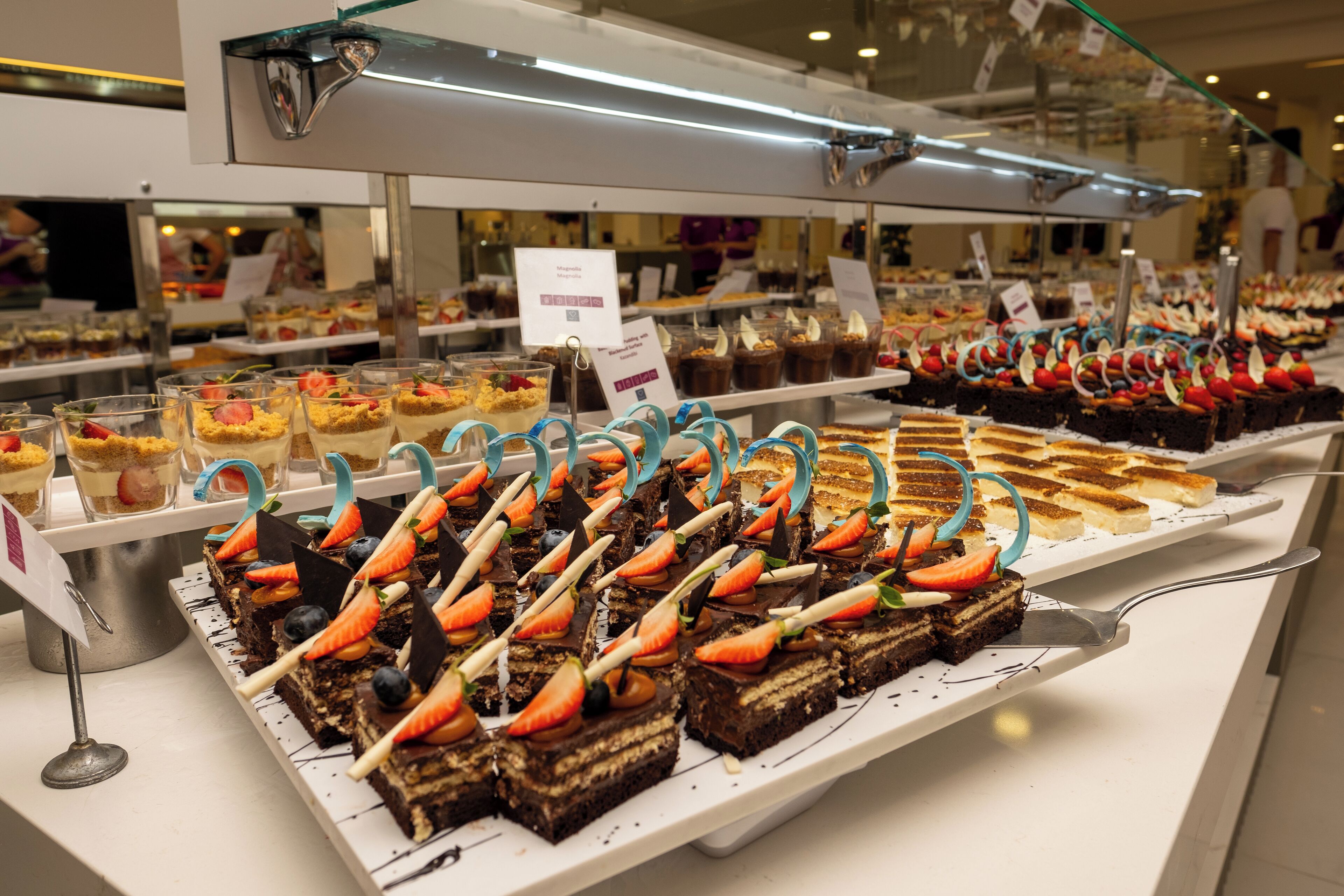 A buffet with various desserts, including cakes and pastries, arranged on white trays.