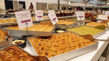 A buffet with various pastries and desserts, including sweet pastry with pistachio in thick syrup and sweet from this tray with coconut flakes.