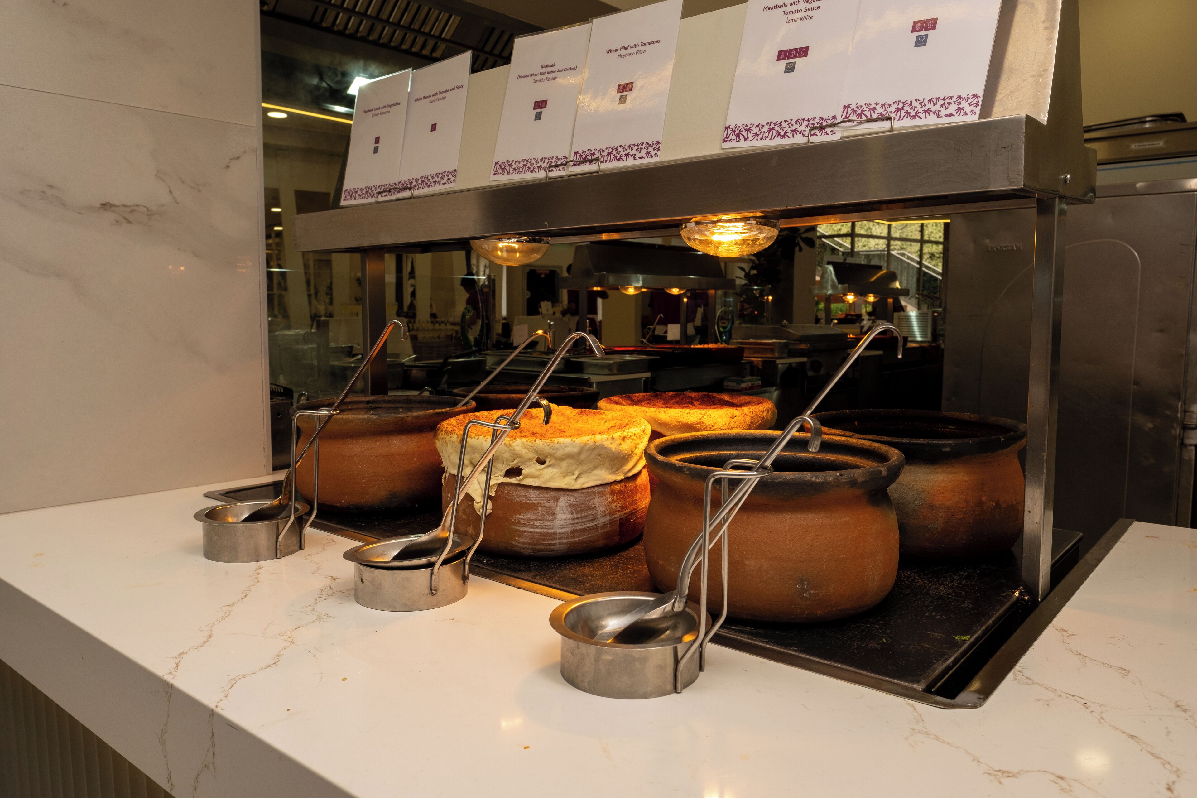 A buffet area with various dishes displayed in pots and bowls, with overhead signage indicating food options.
