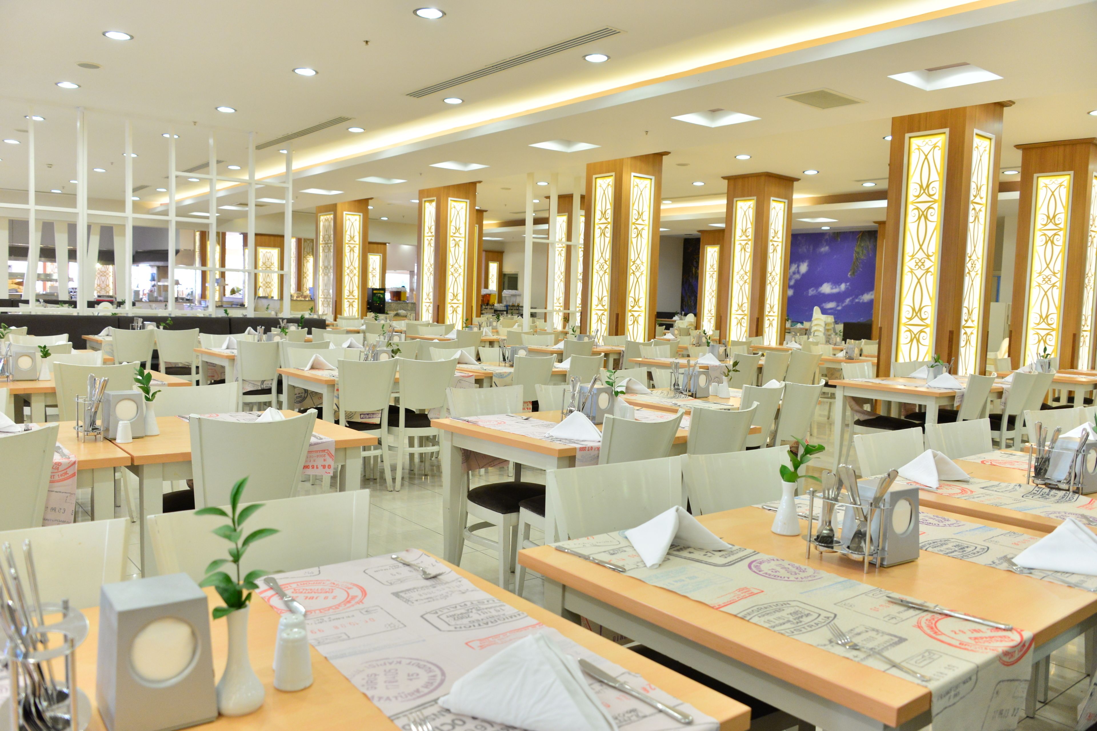 A spacious dining area with multiple tables and chairs, well-lit by ceiling lights, and featuring decorative wooden panels.