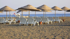 Ein Strand mit Reihen aus weißen Liegestühlen und Strohsonnenhüten.