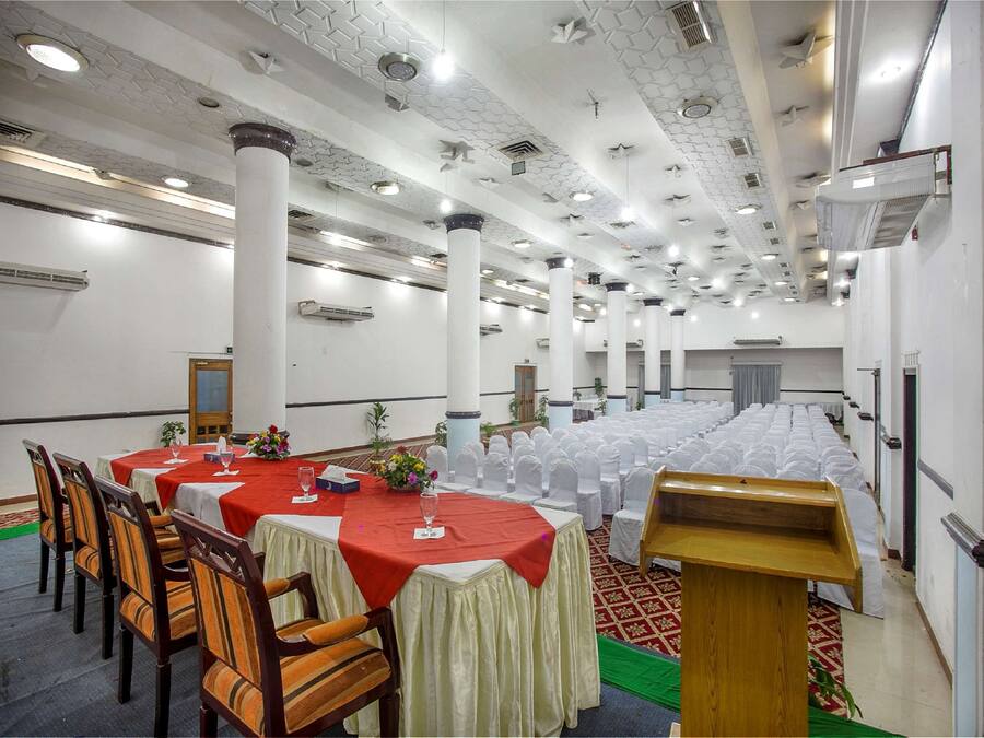 A large banquet hall with rows of tables, white chairs, and a stage area.