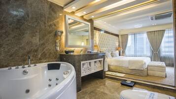 Una habitación de hotel moderna con baño de mármol, una cama grande y una zona de estar separada.