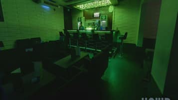 En bar og lounge med en barpræsentation i grønt lys, siddepladser og et ur på væggen.