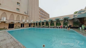 A swimming pool with a tiled deck, surrounded by a building with arched windows and a flat roof. - Hotel Agrabad (Chittagong)