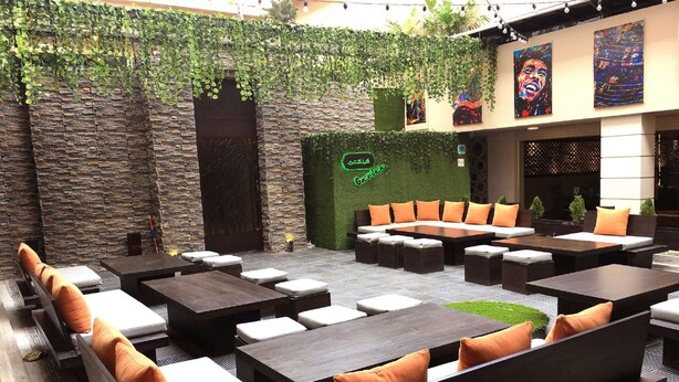 An outdoor seating area with stone walls, green foliage, and orange cushions. - Hotel Agrabad (Chittagong)
