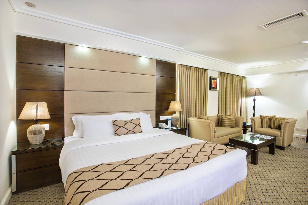 Une chambre d’hôtel avec un grand lit, deux fauteuils, un canapé, une petite table et une table de chevet avec des lampes.