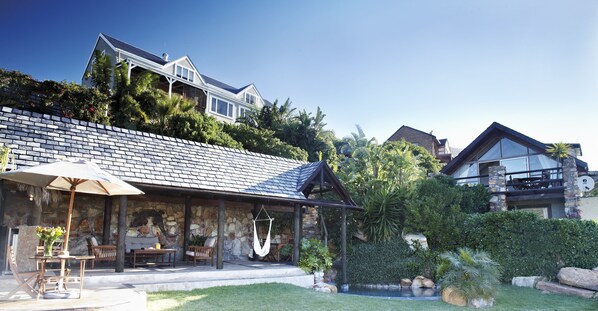 A house with a stone exterior, a patio with outdoor furniture, and a hanging chair. - African Violet Guest Suites (Cape Town)