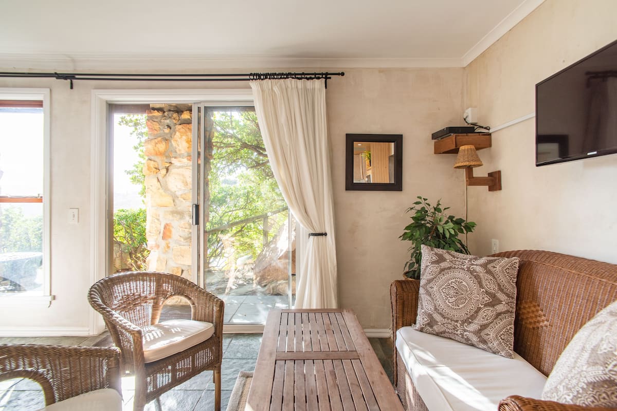 A room with wicker furniture, a wooden table, and a large window with curtains.