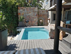 A swimming pool with a stone wall and a barbecue grill. - African Violet Guest Suites (Cape Town)