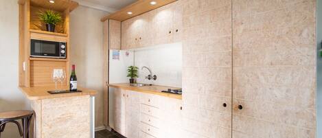Cocina compacta con microondas, lavamanos y encimera de madera.