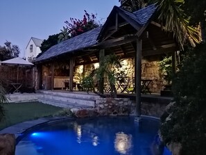 A poolside area with a stone wall, a wooden pergola, and a covered seating area. - African Violet Guest Suites (Cape Town)