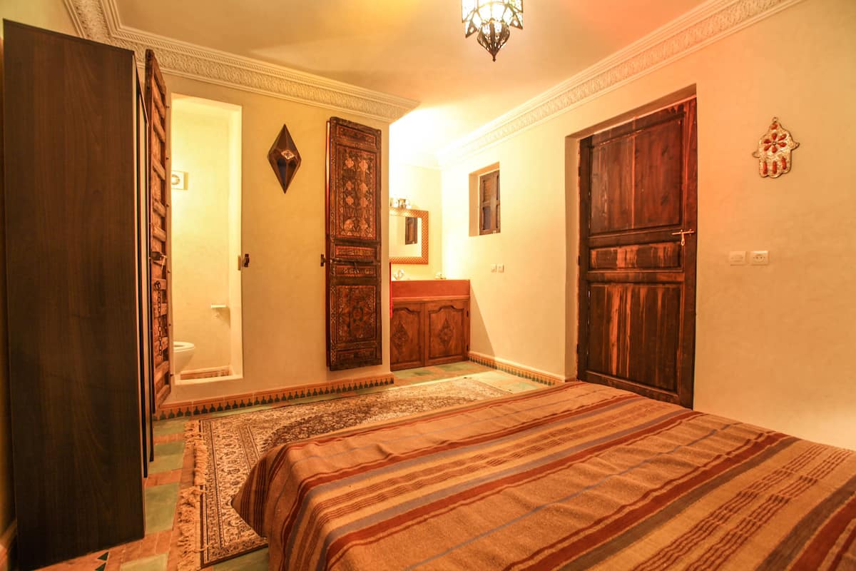 A bedroom with a bed, a wooden wardrobe, a door, and a mirror.