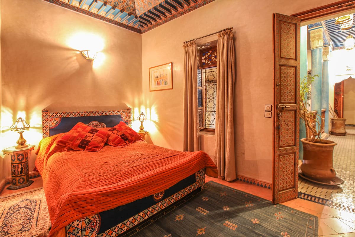 A traditional Moroccan-style bedroom with a large bed, ornate headboard, and a decorative lamp.