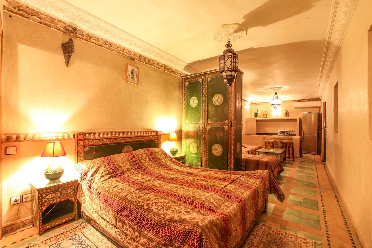A traditional room with a bed, a green cabinet, a small table, and a microwave.