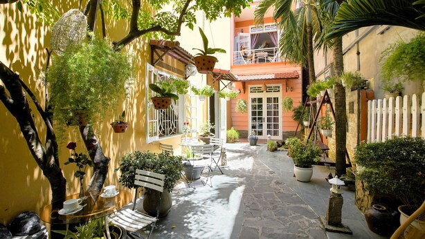 A courtyard with a glass table and chairs, surrounded by potted plants and a white picket fence. - Green Garden Homestay (Da Nang)