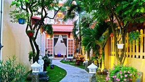 A narrow pathway leading to a building with a red roof and white walls, surrounded by lush greenery and decorative lanterns. - Green Garden Homestay (Da Nang)