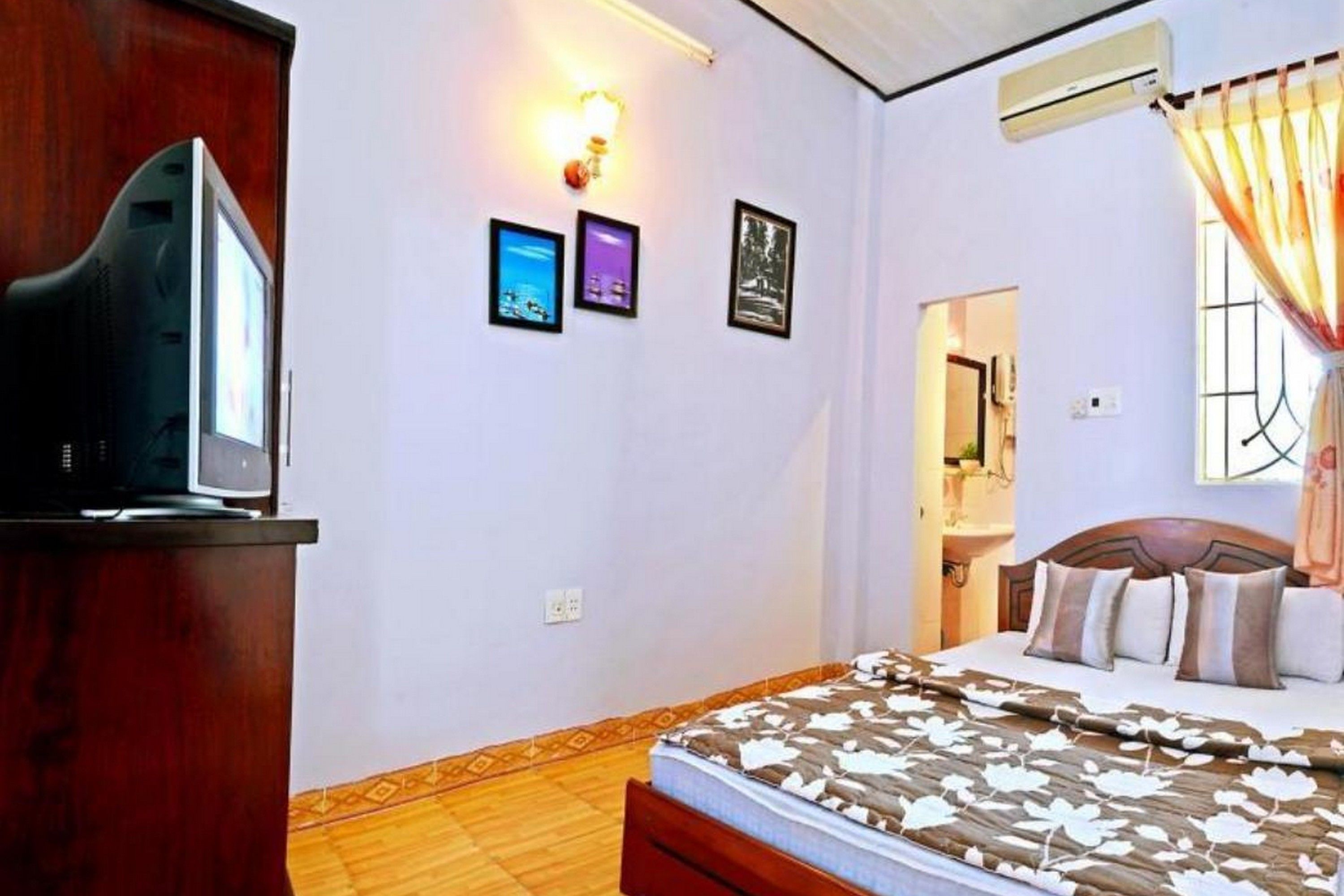 A bedroom with a bed, a television on a stand, and three framed pictures on the wall.