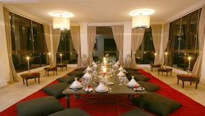 A formal dining room with a long table set for a meal, large windows, and elegant lighting fixtures.