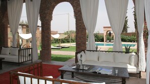 An outdoor seating area with a sofa and table, a pool in the background, and a view of the surrounding landscape.