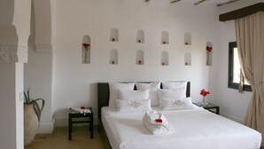 A neatly arranged bedroom with a large bed, multiple pillows, a bedside table with a vase of flowers, and a potted plant.