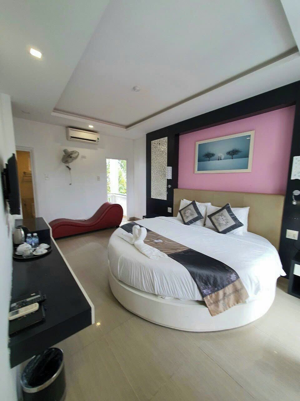 A modern bedroom with a round bed, a red lounge chair, a flat-screen TV, and a painting on the wall.