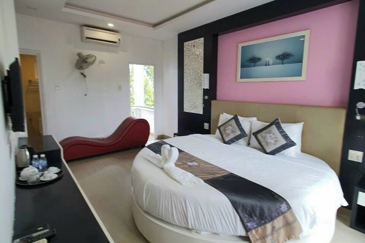 Un dormitorio moderno con cama redonda, una butaca roja, un televisor de pantalla plana y un cuadro en la pared.