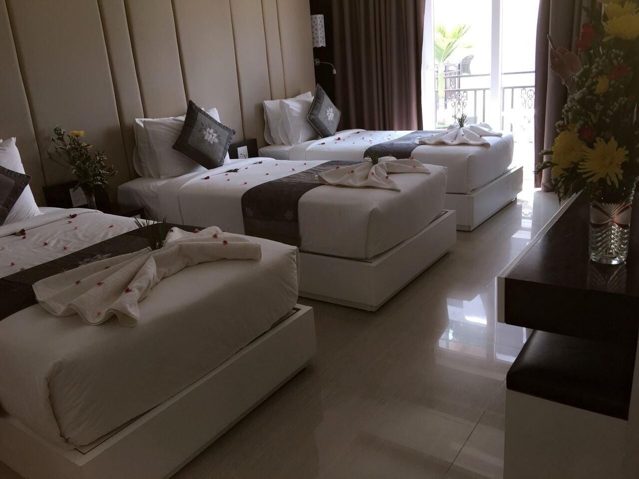 A hotel room with two beds, a small table, and a view of the outdoors.