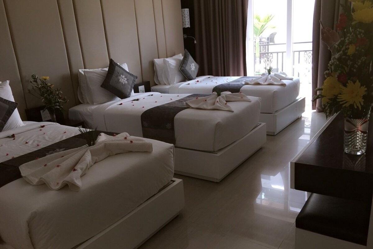 Habitación de hotel con dos camas, una mesita y vistas al exterior.