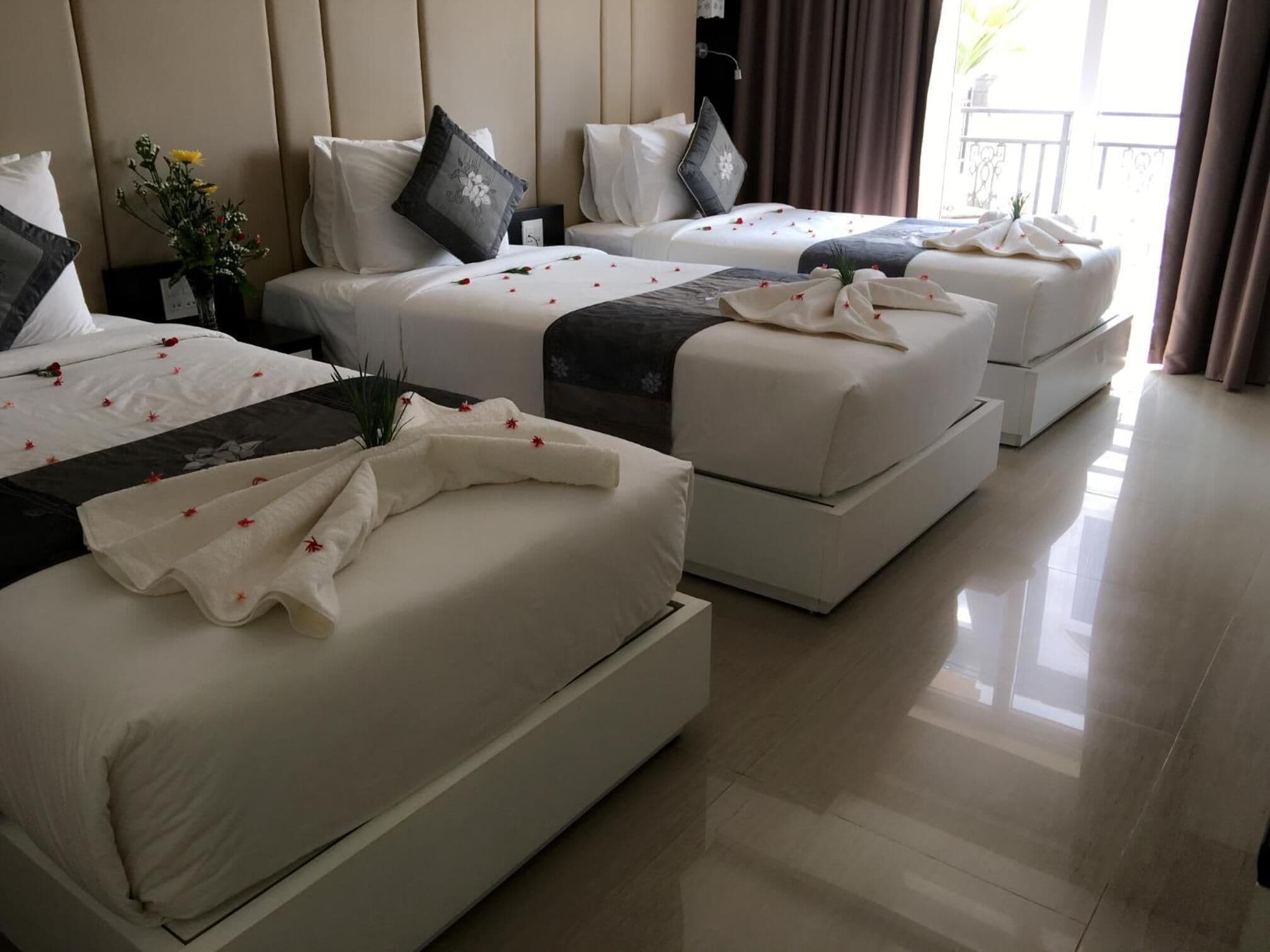 Una camera d'albergo con tre letti allineati, ognuno con biancheria bianca e cuscini decorativi.