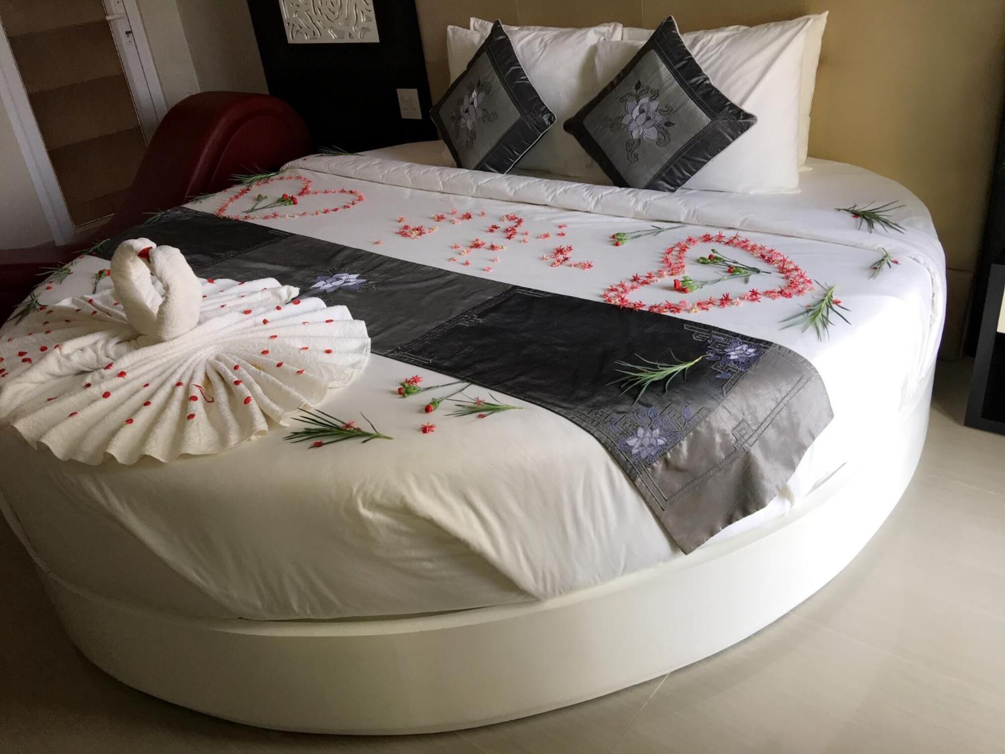A round bed with a white and gray bedspread, decorative swan, and floral arrangements.