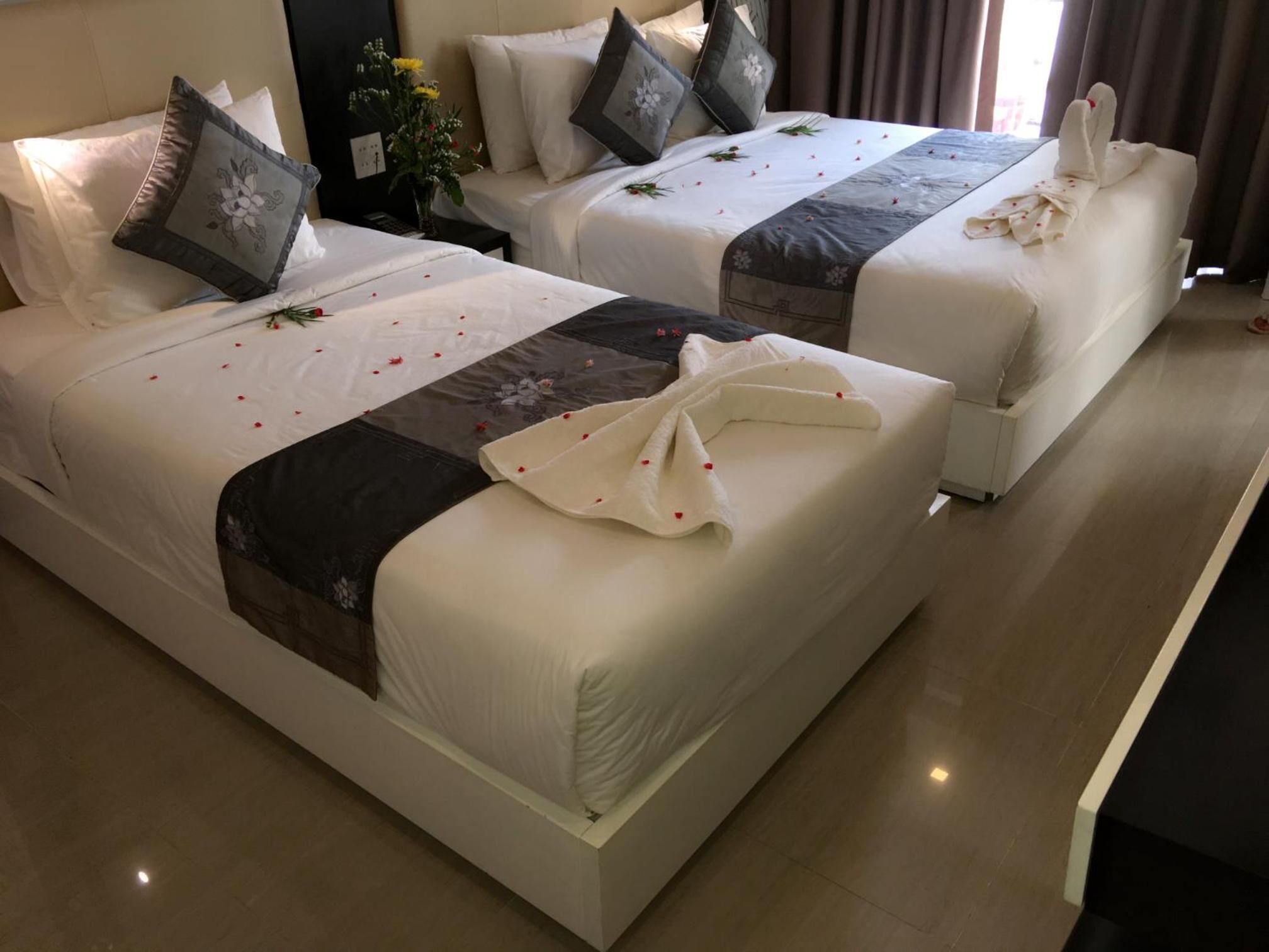 Two neatly made beds with white linens, a dark patterned bedspread, and decorative pillows.