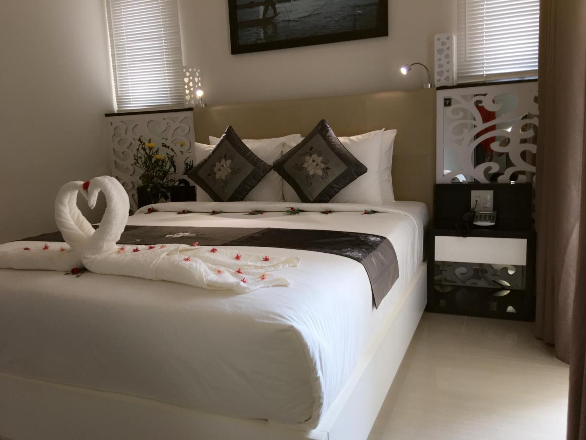 A neatly made bed with a swan towel decoration, two decorative pillows, and a bedside table with a lamp.