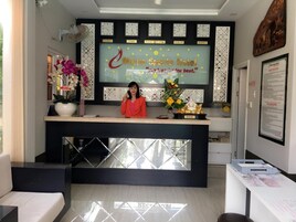 A hotel reception desk with a large clock displaying times for various cities, a receptionist, and a decorative wall with flowers and a slogan.