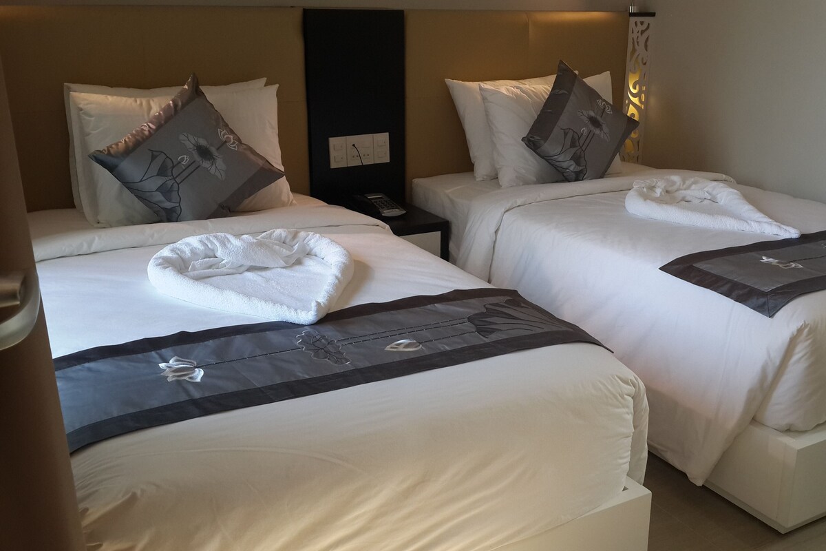 Una habitación de hotel con dos camas, cada una con una colcha blanca y un corredor decorativo oscuro.