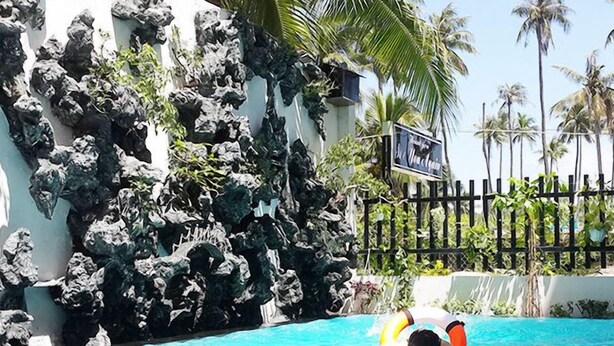 A pool area with a rocky wall, palm trees, and a sign that reads "La Quinta". - Mui Ne Sports Hotel (Mui Ne)