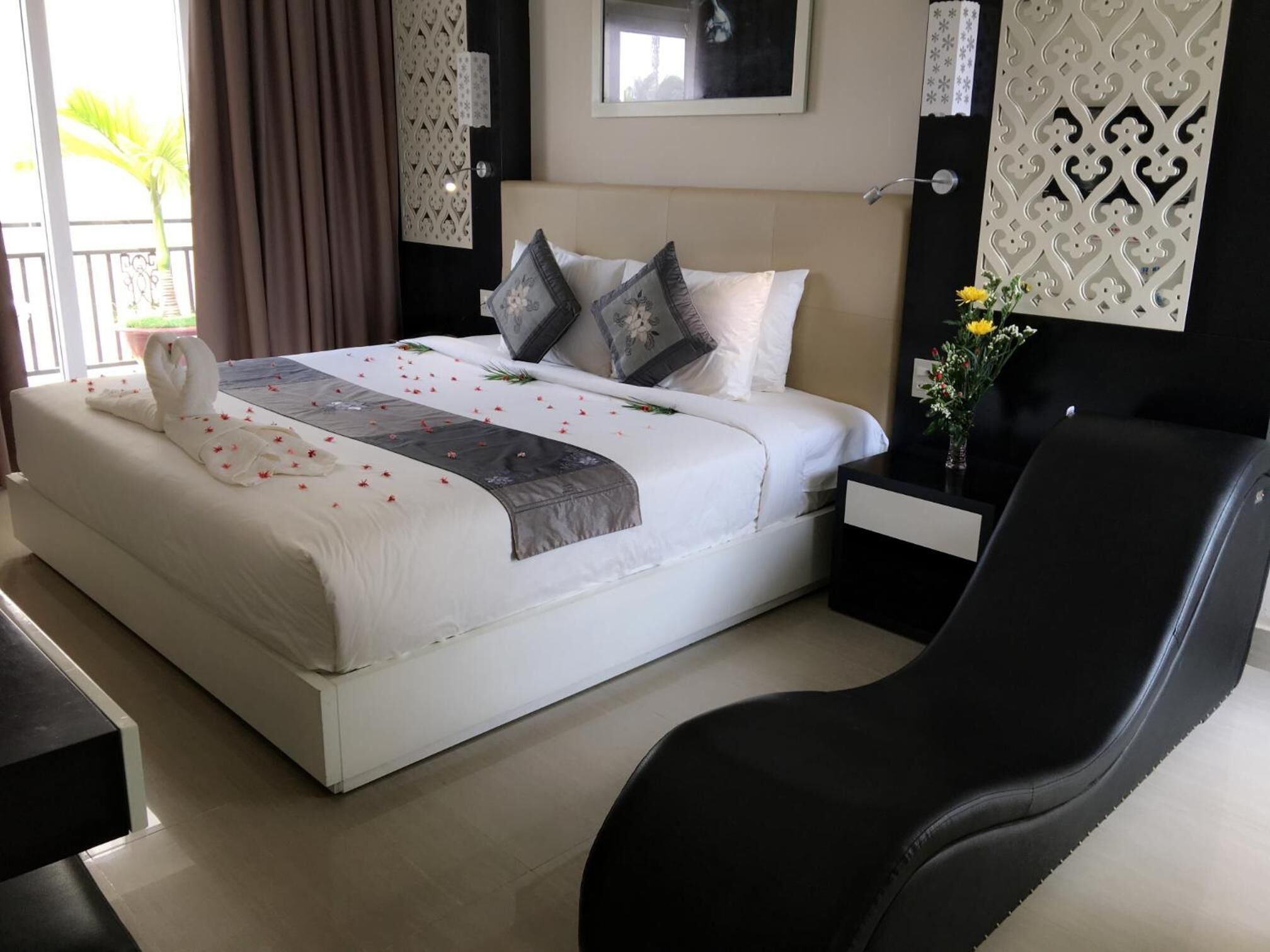 A hotel room with a large bed, a black leather chair, a nightstand, and a decorative wall panel.