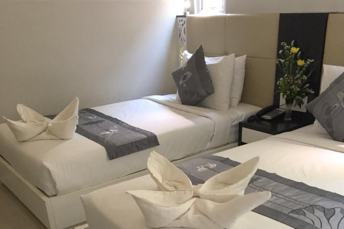 Habitación de hotel con dos camas, cada una con una almohada y una toalla doblada.
