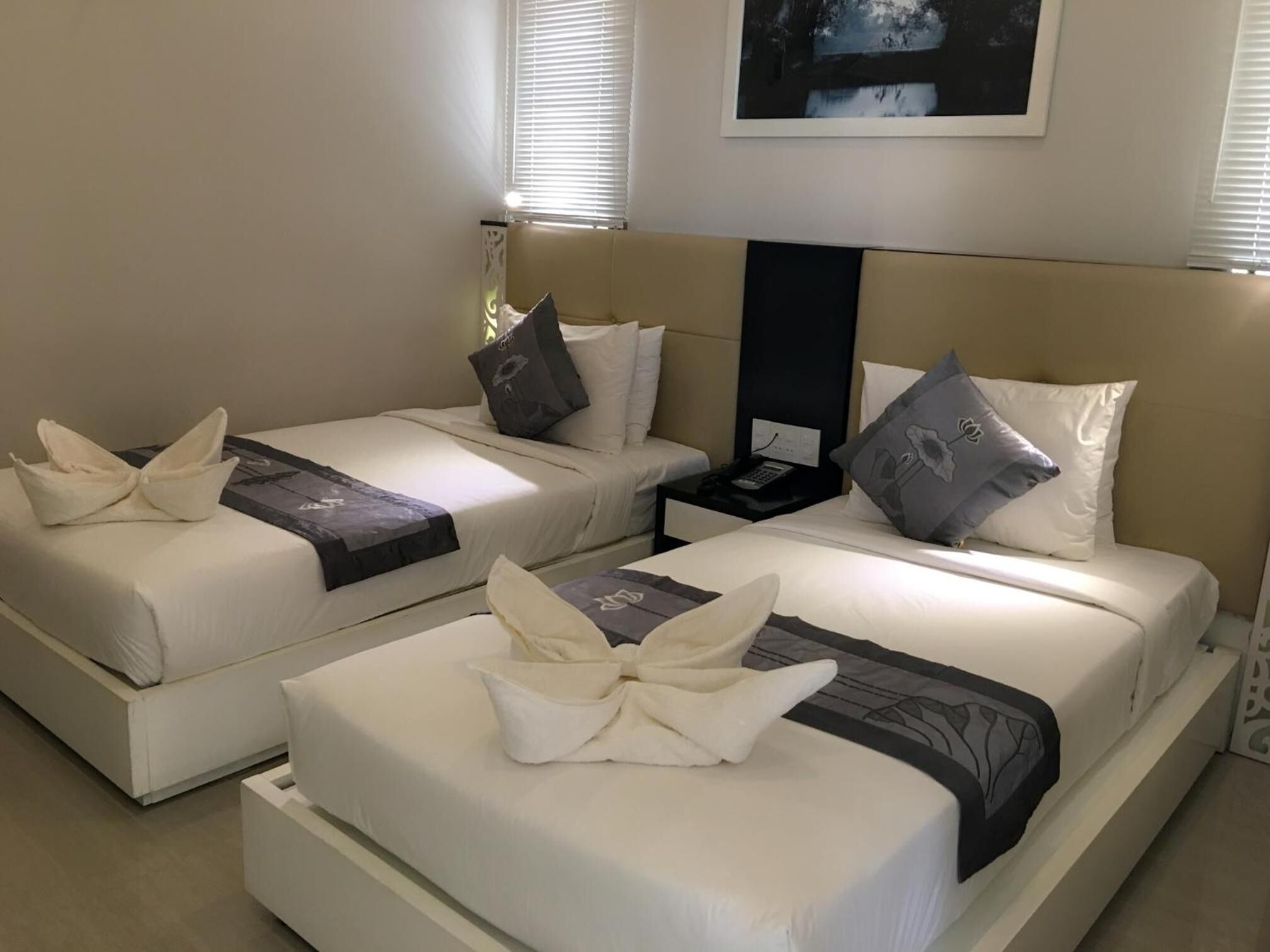 Une chambre d’hôtel avec deux lits, chacun agrémenté de draps blancs et de coussins décoratifs. On y trouve une table de chevet avec un téléphone et une petite table entre les deux lits.