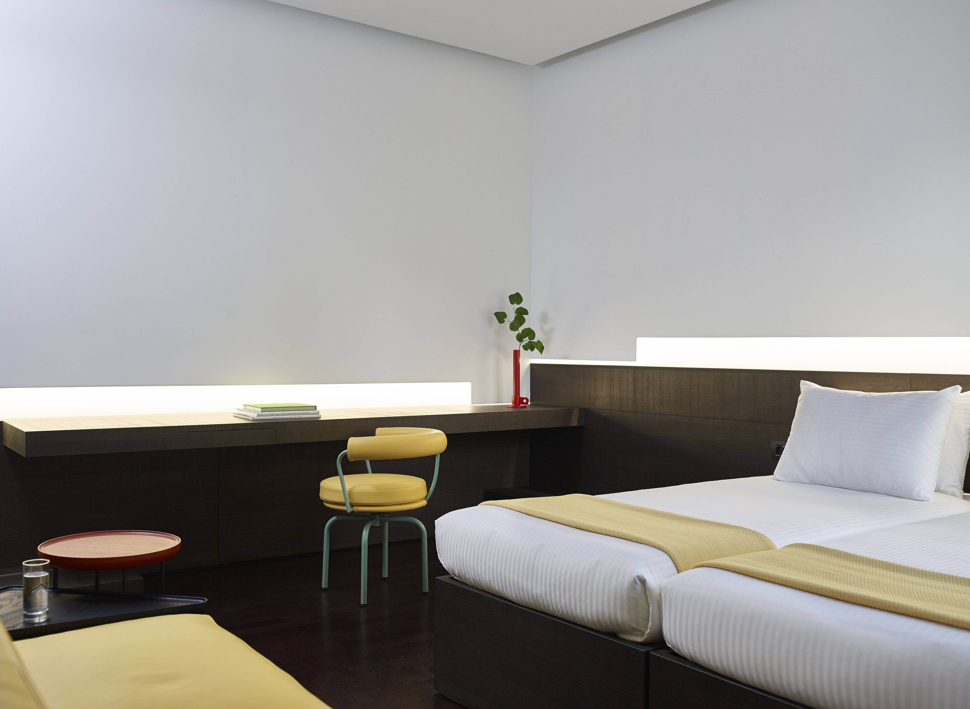 A modern hotel room with a large bed, a small desk, a chair, and a bedside table.