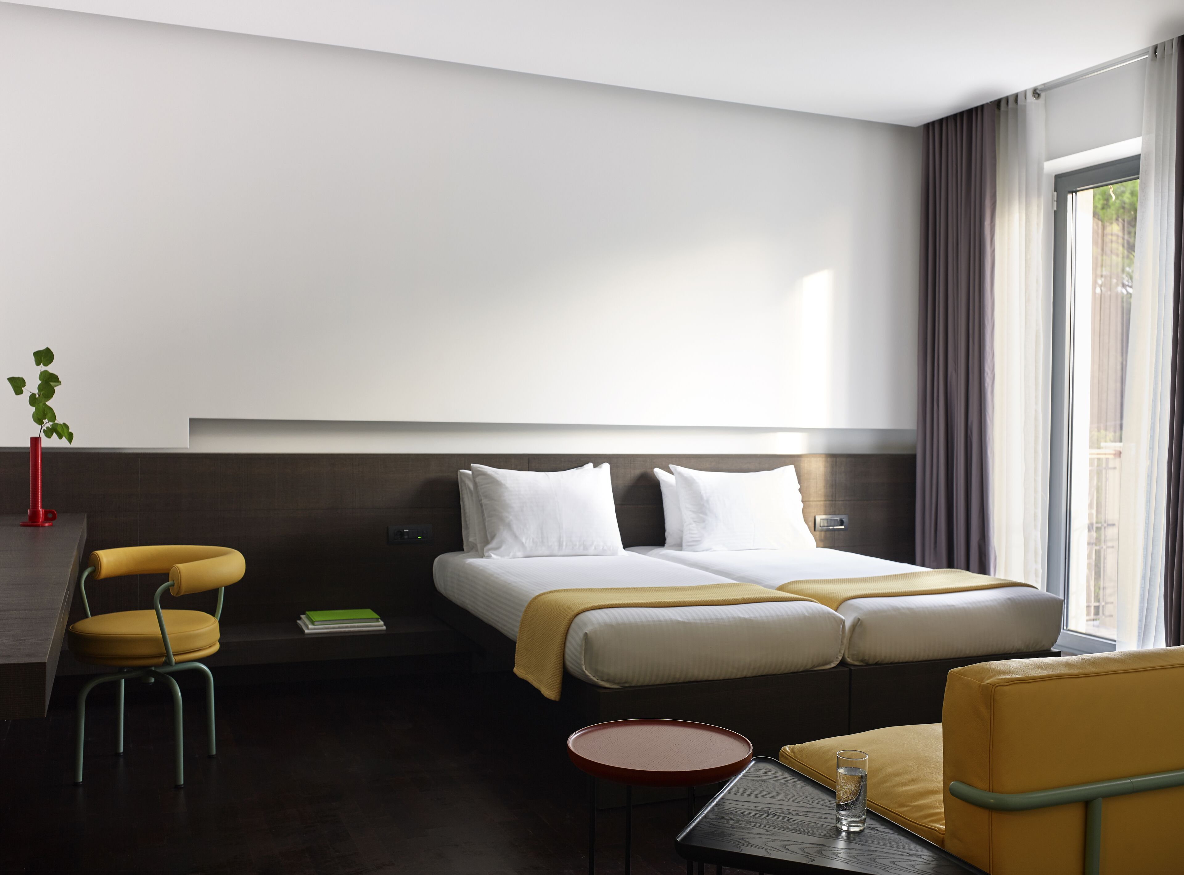 A hotel room with a bed, a chair, a small table, and a window.