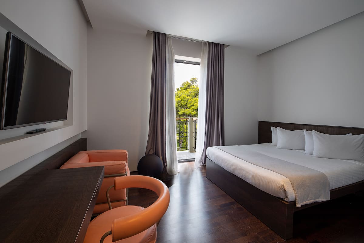 A hotel room with a bed, a TV, a desk, and a view of greenery outside.