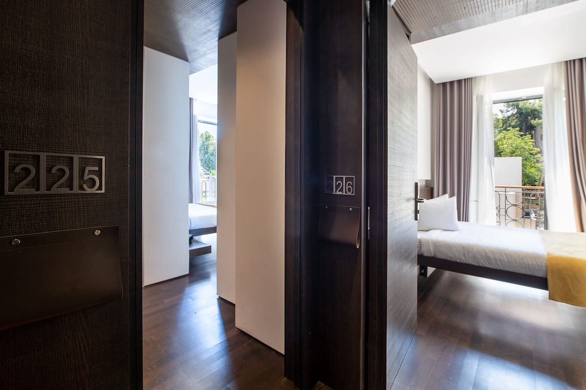 A modern hotel room with a bed, a nightstand, and a view of the outdoors.