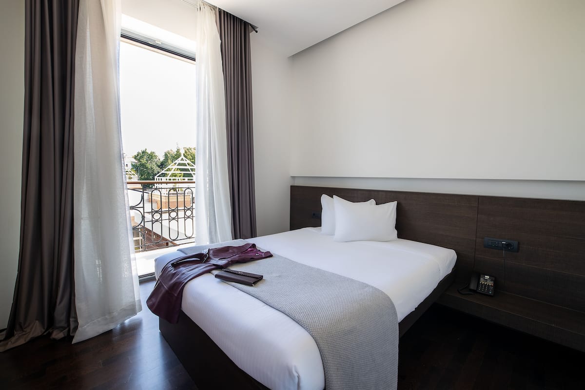 A hotel room with a large bed, a bedside telephone, and a view of a balcony with a railing.